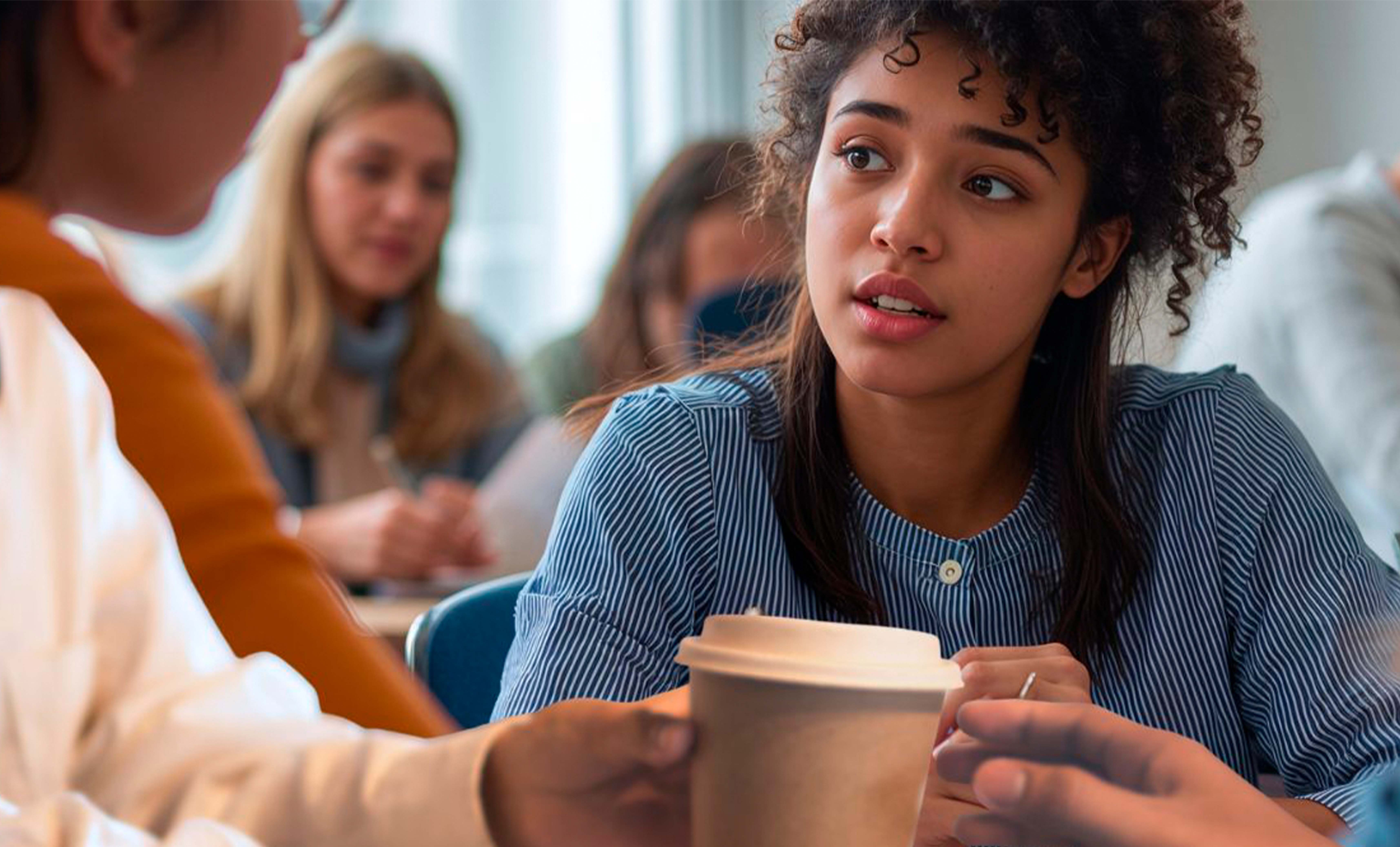 Imagen de una universitaria tomando un café con otras compañeras 